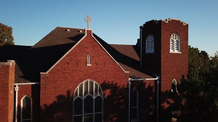 Rotating aerial shot of a red brick church and spire with the sun shining