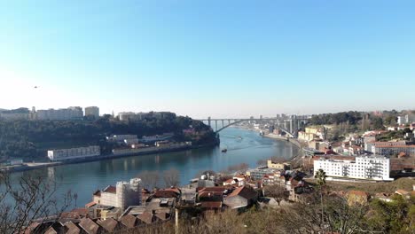 View-from-Crystal-Palace-Gardens-to-Arrábida-Bridge-crossing-Douro-river-in-Oporto,-Portugal---Aerial-Reveal-shot