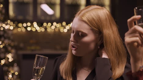 close up view of a red haired girl wearing elegant clothes while talking with her friends and holding a glass of champagne at the new year's party 2