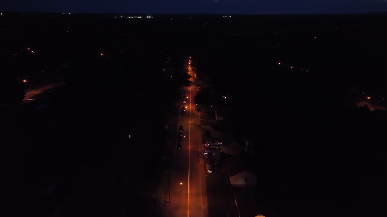 Car on lighting straight street at night. American suburb neighborhood at midnight. Aerial birds eye. Calm peaceful city of USA. Drone wide shot.