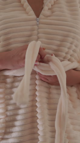 mujer con manicura aprieta el nudo en la túnica en la ducha en un fondo borroso. persona ata el manto de baño de peluche con cinturón después de tomar la ducha en cámara lenta