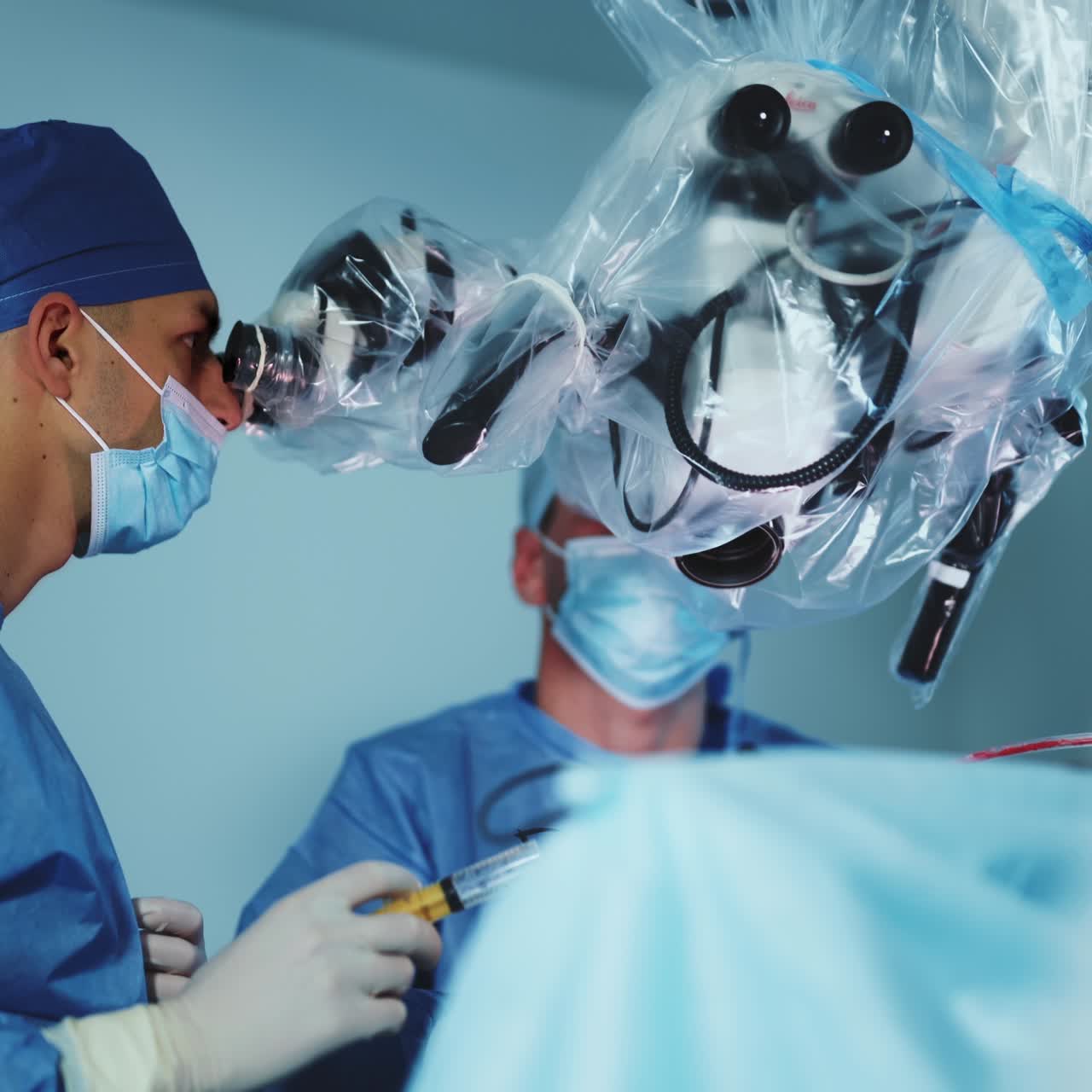Focused doctor in mask and cap holding a syringe and looking at microscope. Present-day surgery using advanced equipment