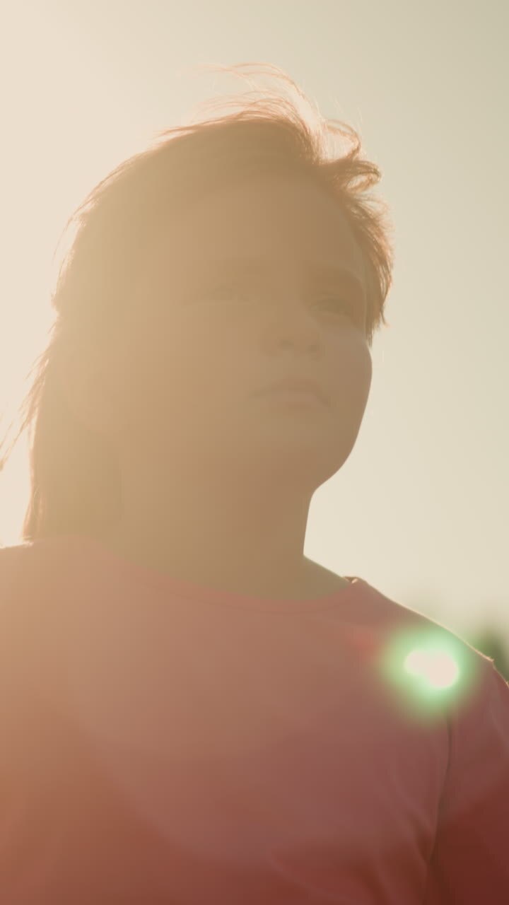 Little girl in pink shirt looking thoughtful under bright sunlight with partial view of adult standing near her, sunlight creates glowing effect around them, giving scene warm and serene vibe