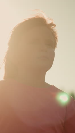 little girl in pink shirt looking thoughtful under bright sunlight with partial view of adult standing near her, sunlight creates glowing effect around them, giving scene warm and serene vibe