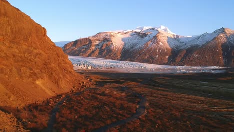 drone establishing shot of two brave explorers hiking on lonely trail towards the snaefellsjokull glacier in south coast of iceland on a golden light bathed landscape and snow capped rugged mountains