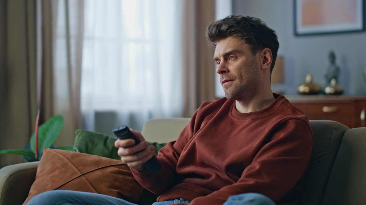 Ragazzo nervoso che cambia i canali televisivi sul divano con il telecomando, in primo piano.