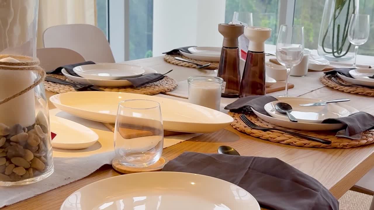 A stylish dining table featuring neutral-toned plates, cutlery, and decor with a serene backdrop.