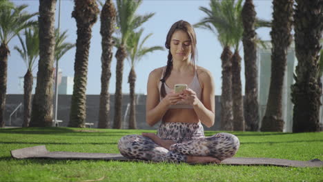 Mujer-Sentada-En-Pose-De-Loto-Con-Teléfono-Inteligente.-Chica-Usando-Celular-En-El-Parque