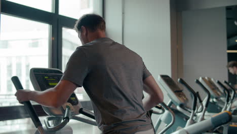 Fit-man-warming-up-in-sport-club.-Male-athlete-using-elliptical-trainer-at-gym