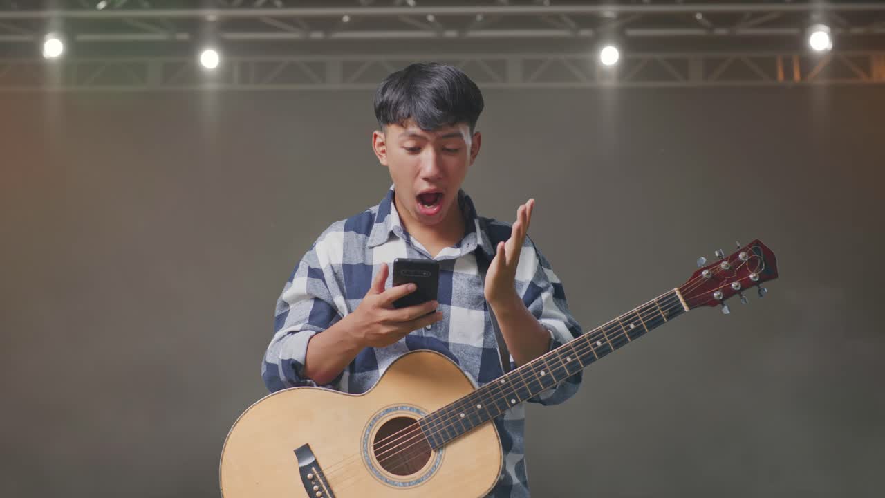스마트폰을 사용하고 무대에 서서 와우라고 말하는 기타를 들고 있는 아시아 십대