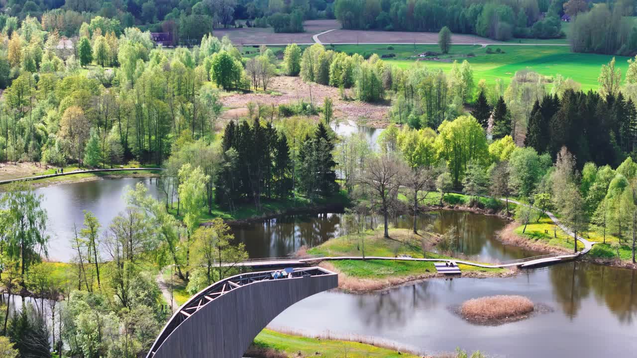A Scenic View From the Kirkilai Observation Tower Reveals Winding Boardwalks, Tranquil Karst Lakes, and Lush Forested Surroundings in Biržai Regional Park, Lithuania - Aerial Pullback Shot