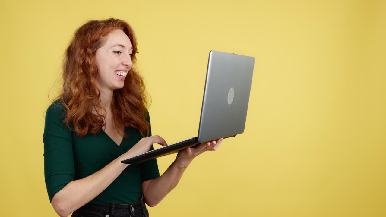 Happy redhead woman using a laptop with a yellow background