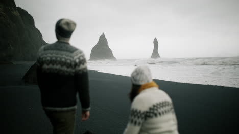 couple walking on a black sand beach in iceland