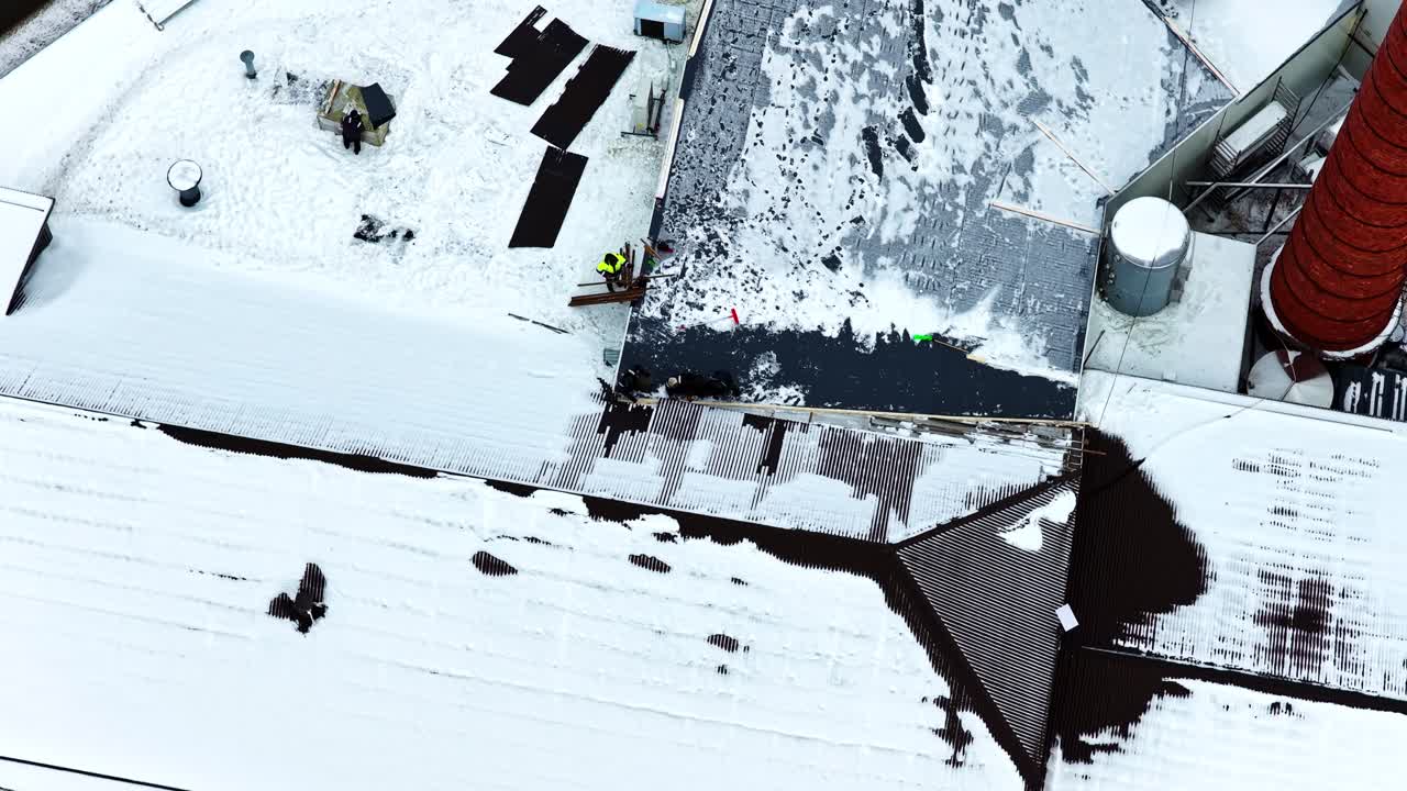 Roofers repairing commercial building roof after snow, maintenance specialists at height