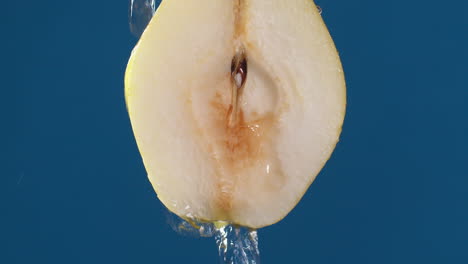 yellow half pear on a blue dark background with drops of water rolling down the pear and flowing splashing with isolated background