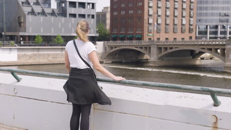 young woman taking in the view from a bridge over a river in a downtown, urban environment