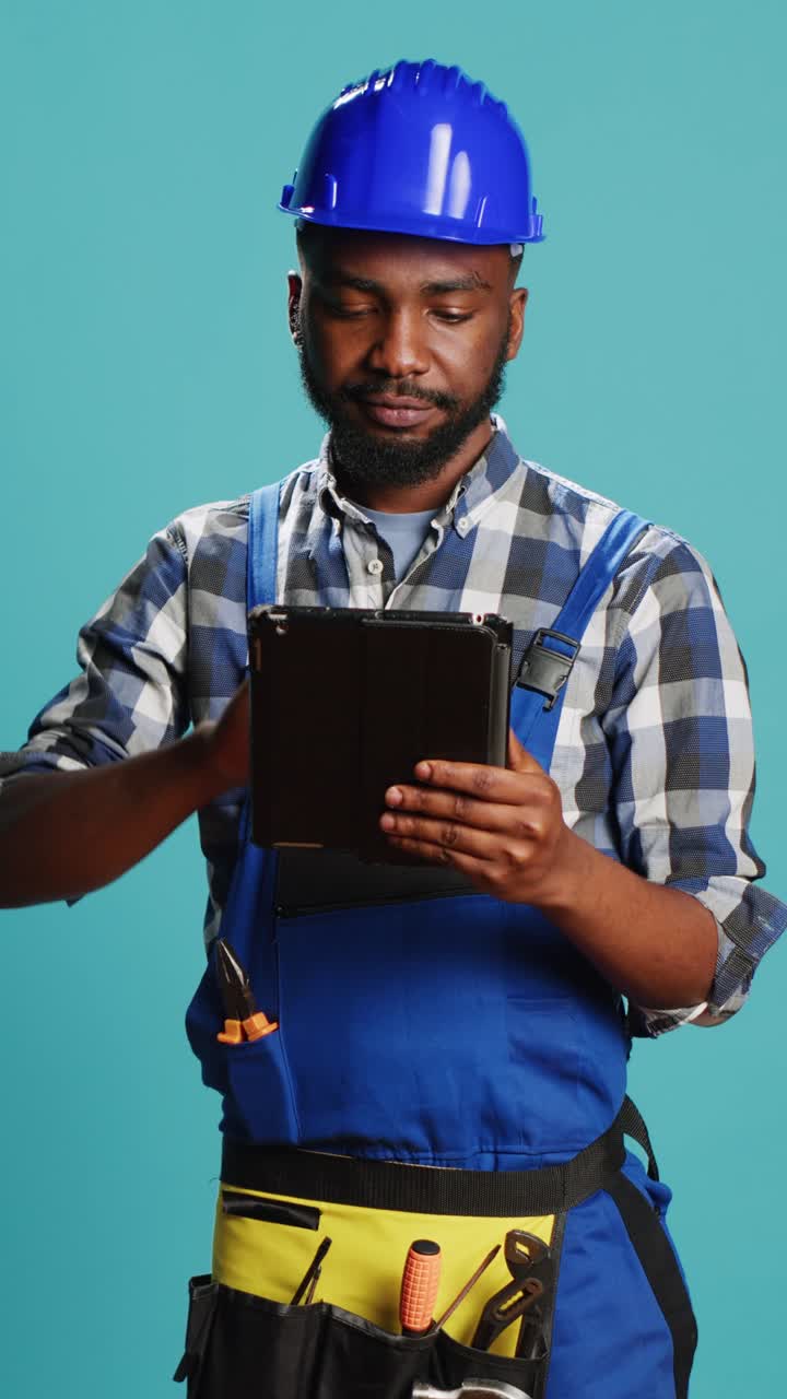 Vertical video: Young handyman using digital tablet on camera