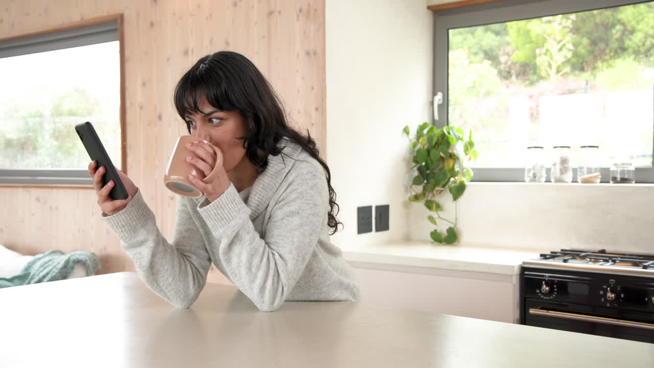 Smiling woman using smartphone voice message while holding coffee mug at home, copy space