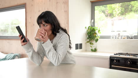 smiling woman using smartphone voice message while holding coffee mug at home, copy space
