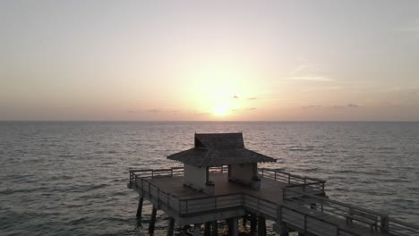 slow rising aerial of empty fishing pier on calm empty ocean at sunset