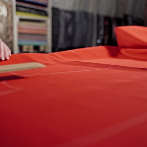 woman tailor is working at table with red cloth in atelier. skilled seamstress is drawing sketch lines with a soap or a chalk and a ruler on red fabric.