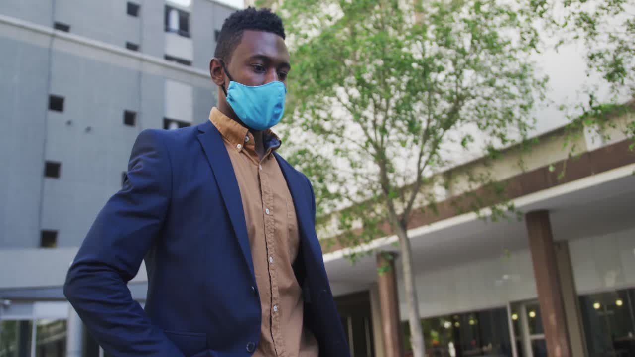 hombre de negocios afroamericano con máscara facial usando un teléfono inteligente en la calle