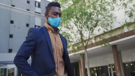 hombre de negocios afroamericano con máscara facial usando un teléfono inteligente en la calle