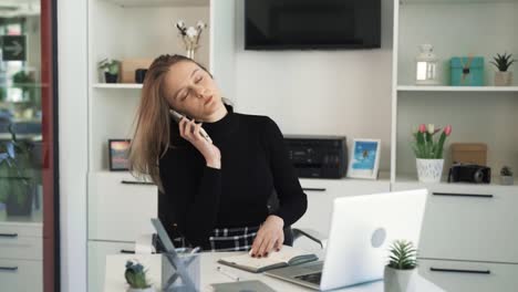 Die-Junge-Frau-Arbeitet-An-Ihrem-Laptop,-Macht-Multitasking-Und-Erhält-Einen-Anruf,-Der-Sie-Von-Ihrer-Arbeit-Ablenkt.-Sie-Ist-Mit-Der-Unterbrechung-Nicht-Zufrieden,-Sie-Arbeitet-In-Einem-Büro