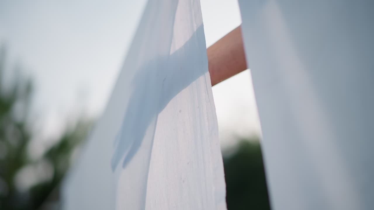 Gentle breeze causes homeowner to fix laundry. Sunlit setting prompts resident to reposition clothes on line. Outdoor sunlight and breeze motivate homeowner to adjust hanging fabric