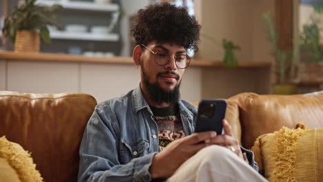 hombre sonriente usando su teléfono en el sofá