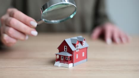 person inspecting a model house with a magnifying glass