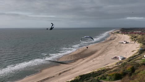 Paragliders-Flying-Over-Moody-Overcast-Beach,-Wide-Angle-Aerial-Shot,-Zeeland