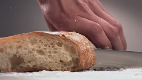 extreme cu super slow motion caucasian male cutting loaf of bread on a wooden table in bakery. shot with high speed camera at 420 fps