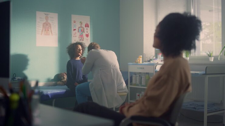 Pediatrician examining girl throat. Mom sitting waiting on medical consultation.