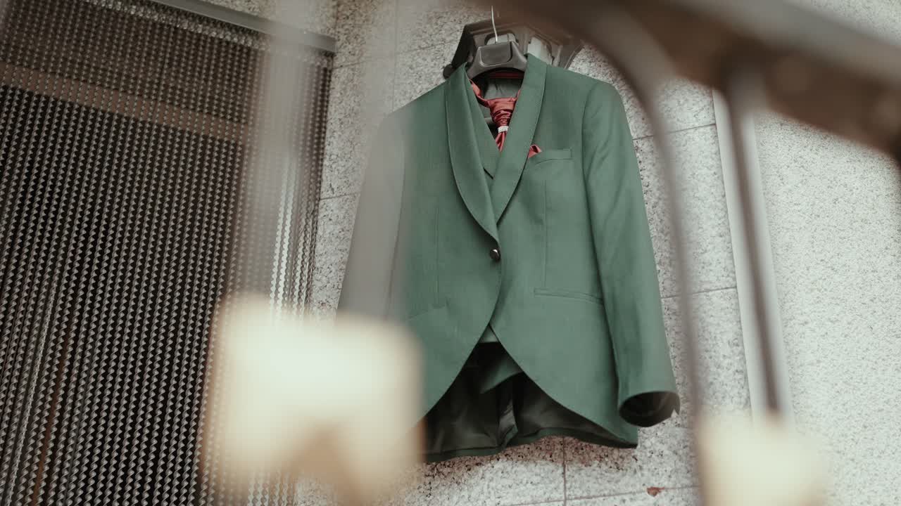 green groom suit with red tie and pocket square hanging on wall before wedding ceremony