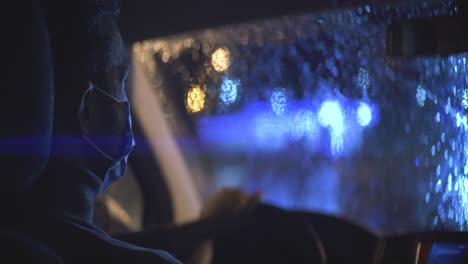 the young man in medical mask is sitting in the car on the rainy evening