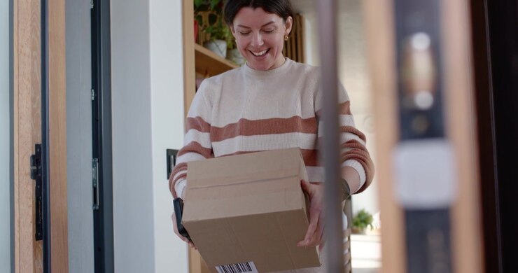 Woman spotting cardboard box with barcode on dark mat, lifting parcel, entering hall