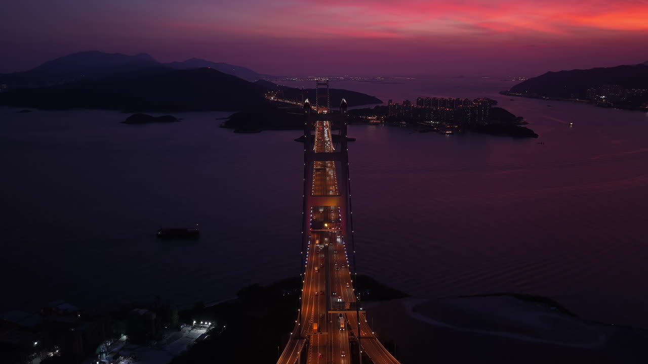 Cinematic Aerial view of Tsing Ma Bridge in Hong Kong at sunset, spanning over calm waters with city skyline, mountains, and ships in the distance, creating a serene urban and natural landscape scene