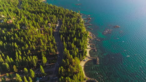 pine tree forest growing on the shore of lake tahoe, california, usa. highway through the woods with cars on. amazing blue of the lake with boats on.