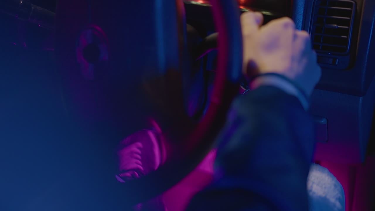 Interni di un veicolo di notte illuminati con luci colorate e vivaci. Suggestiva scena urbana con un conducente che stringe con forza il volante durante le ore notturne, con un'illuminazione dinamica viola e blu.