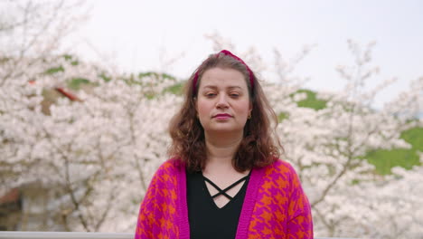 Female-Traveler-Looking-Up-To-Camera-With-Cherry-Blossoms-In-Background