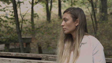 Slider-dolly-shot-of-millennial-female-sitting-on-a-park-bench-and-looking-at-trees