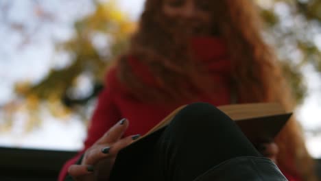 Portrait-Of-Pleased-Young-Lady-With-Long-Curly-Red-Hair-Sitting-On-Bench-And-Reading-Book-In-Park