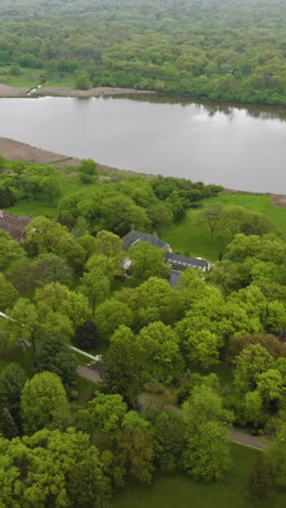 little pond surrounded by green trees and grassy lawns. private houses at the beautiful waterfront on summer day. top view. vertical video