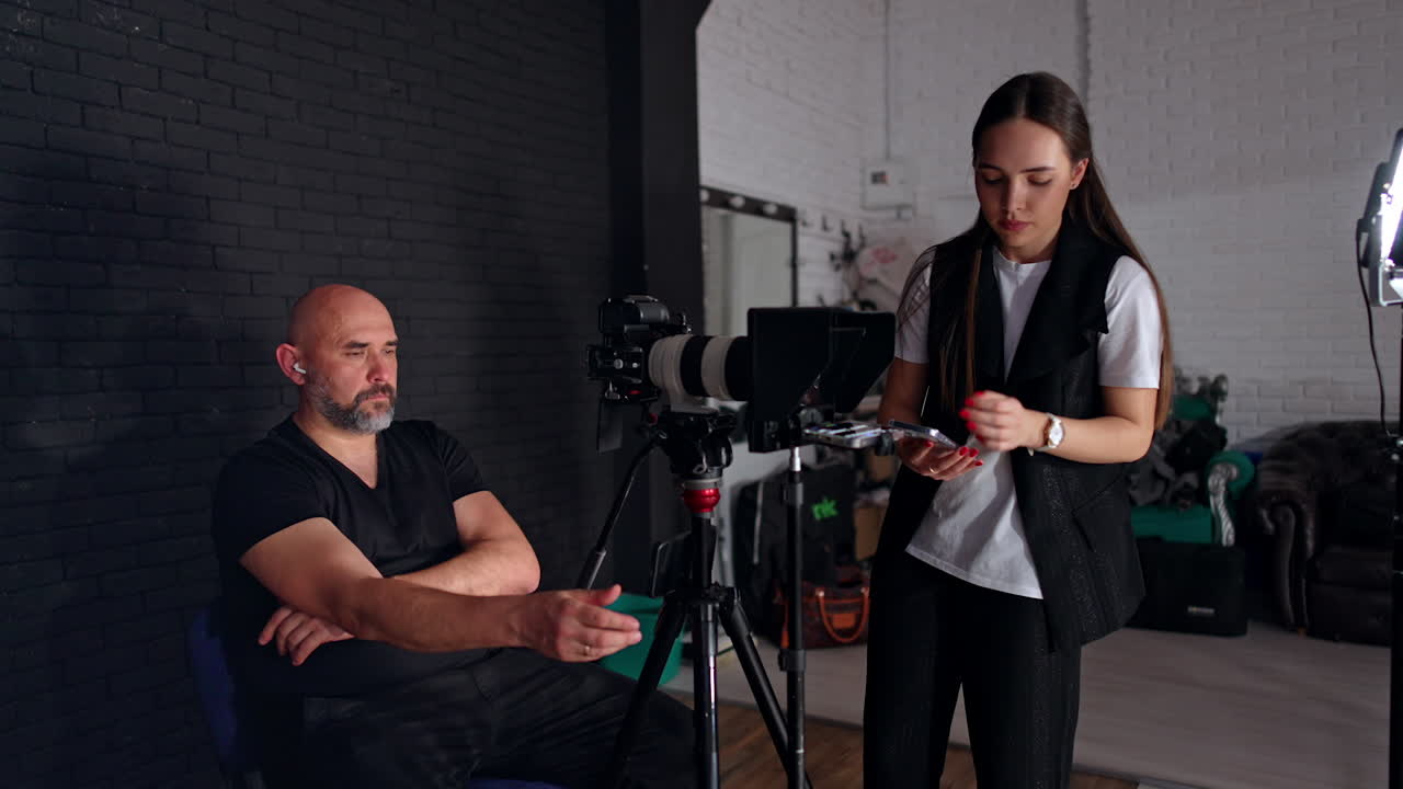 People working backstage in modern photo studio. Cameraman and brunette girl taking a video.