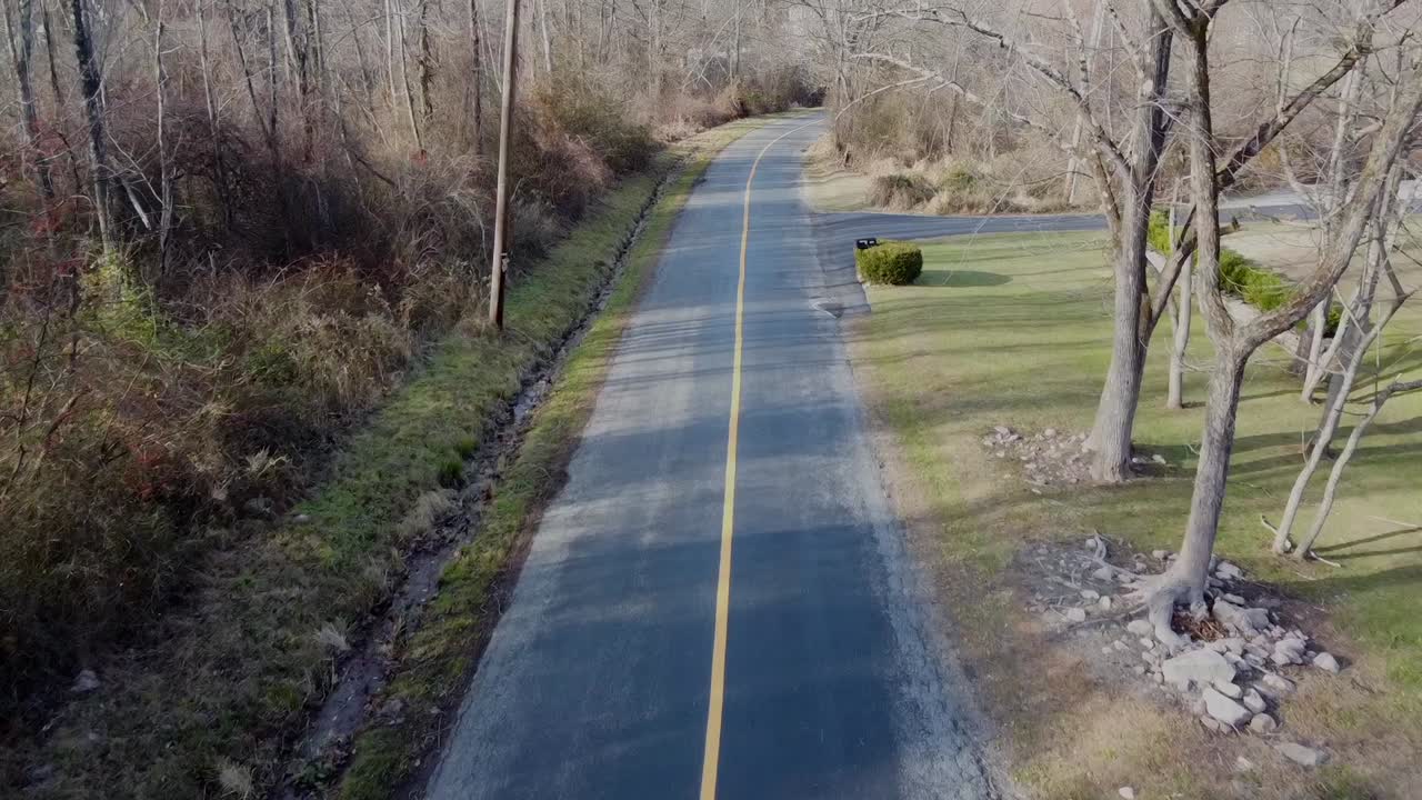 노란색 선이 있는 도로를 따라 비행하는 드론과 잎이 없는 나무와 작은 수로도 볼 수 있습니다.