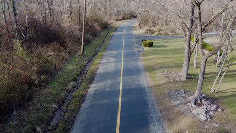 Drone-Volando-A-Lo-Largo-De-Un-Camino-Con-Una-Línea-Amarilla-También-Puedes-Ver-árboles-Sin-Hojas-Y-Un-Pequeño-Barranco-De-Agua