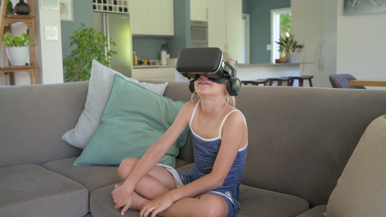 Adolescente con gafas de realidad virtual reaccionando a la RV, girando, estirándose y sonriendo en el sofá de la sala de estar.