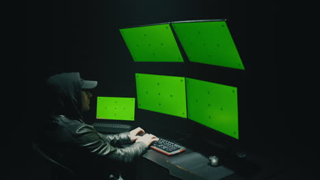 hacker working on multiple green screen monitors in a dark room