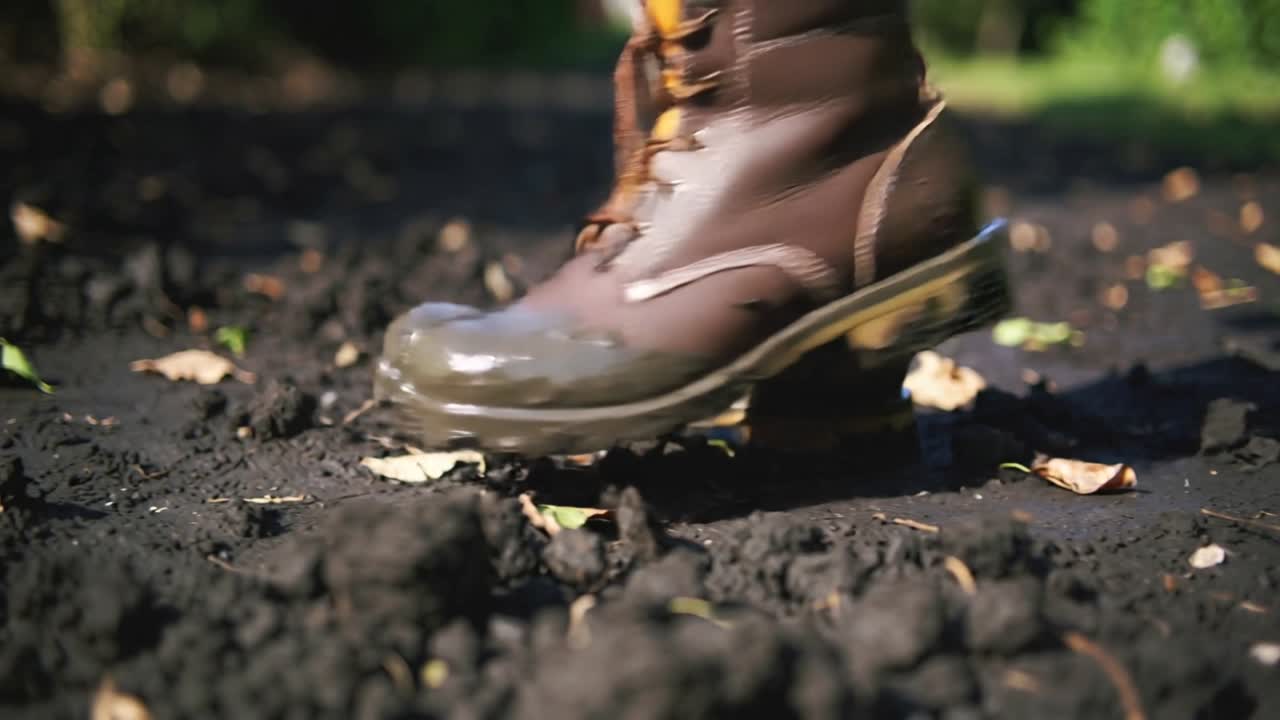 Pressing into ground, brown boots, yellow-collared loose-laced, walking across yard, leaving mud